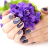 Hands of a woman with dark manicure on nails and bouquet of viol
